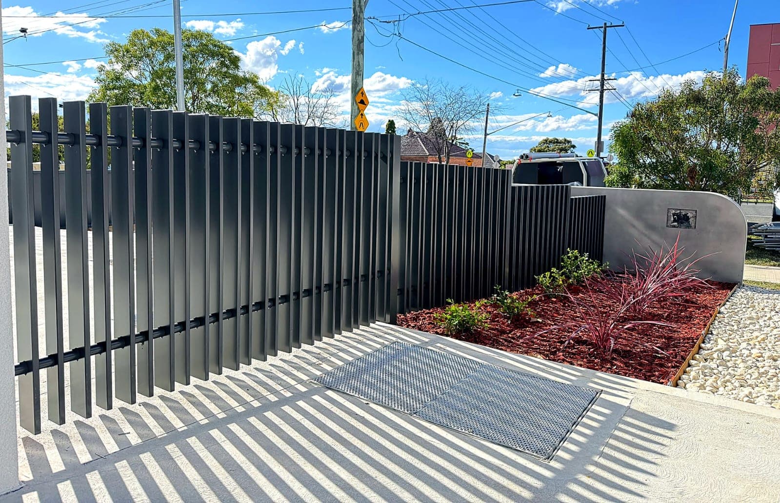 Black vertical-slat metal fence and sliding gate beside a landscaped path